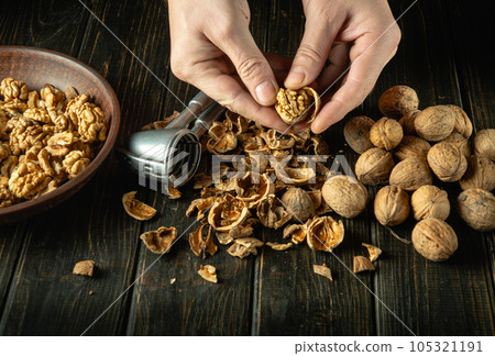 The cook is peeling walnuts on the kitchen table. Close-up of the chef hands while working. Culinary concept on dark background 105321191