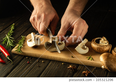 The chef hands cut mushrooms with a knife on a kitchen cutting board before preparing a vegetarian dinner with herbs and spices. Copy space 105321206