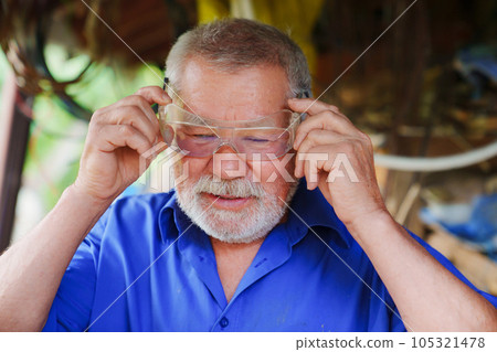 an elderly man in goggles to work with a circular saw 105321478