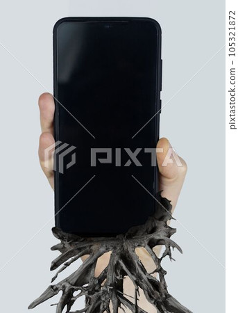 Man holds a smartphone in his hand, from which roots have escaped and dig into his hand. Concept shot of smartphone addiction. Loss of ability to live normal life.  Negative impact of digitalization 105321872