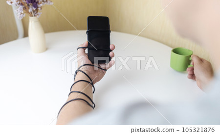 Overcoming phone addiction. Man hand is wrapped around the wire of smartphone charger. Conceptual photo of smartphone addiction. Loss of ability to live normal life. Negative impact of digitalization Overcoming phone addiction. Man hand is wrapped around the wire of smartphone charger. Conceptual photo of smartphone addiction. Loss of ability to live normal life. Negative impact of digitalization 105321876