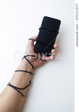 Overcoming phone addiction. Man hand is wrapped around the wire of smartphone charger. Conceptual photo of smartphone addiction. Loss of ability to live normal life. Negative impact of digitalization Overcoming phone addiction. Man hand is wrapped around the wire of smartphone charger. Conceptual photo of smartphone addiction. Loss of ability to live normal life. Negative impact of digitalization 105321877
