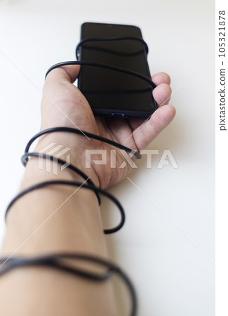Overcoming phone addiction. Man hand is wrapped around the wire of smartphone charger. Conceptual photo of smartphone addiction. Loss of ability to live normal life. Negative impact of digitalization 105321878