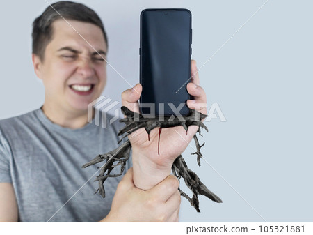 Man holds a smartphone in his hand, from which roots have escaped and dig into his hand. Concept shot of smartphone addiction. Loss of ability to live normal life.  Negative impact of digitalization 105321881