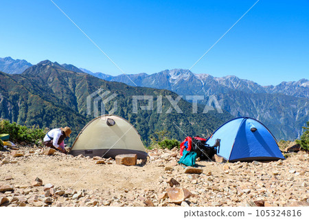 View of the Reike Sanso tent site on the ridgeline of Mt. Kashima Yarigatake in the Northern Alps and a female climber setting up a tent 105324816