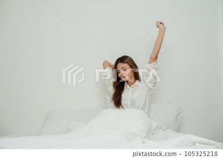 Beautiful asian woman stretching in bed with her arms raised Beautiful asian woman stretching in bed with her arms raised 105325218