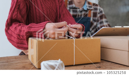 Couple small business owner working with computer at workplace. Couple business seller check product order. Packing goods for delivery to customer. Online selling. E-commerce. Shipping concept Couple small business owner working with computer at workplace. Couple business seller check product order. Packing goods for delivery to customer. Online selling. E-commerce. Shipping concept 105325258