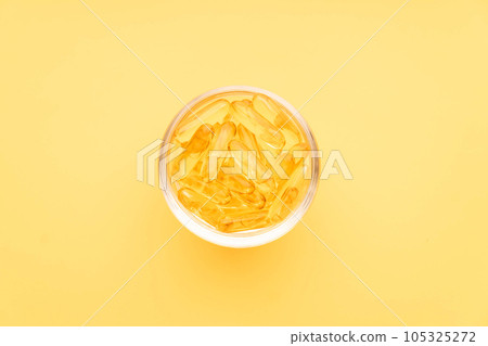 Oil softgel capsules in glass bowl on yellow background. Nutritional supplement contains fish oil, omega 3, omega 6, omega 9, vitamin e, vitamin d and vitamin a. Top view. Oil softgel capsules in glass bowl on yellow background. Nutritional supplement contains fish oil, omega 3, omega 6, omega 9, vitamin e, vitamin d and vitamin a. Top view. 105325272