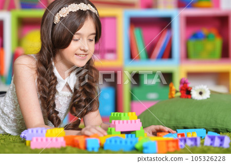 Portrait of cute girl playing with colorful plastic blocks in room 105326228
