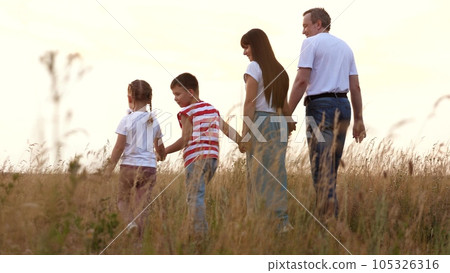 Happy family with adorable little children walks across field at sunset light backside view. Children enjoy spending time with loving parents on family holiday. Family with children rest at rural side 105326316