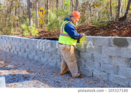 During development of new property, construction worker is using cement blocks for building retaining wall. 105327180