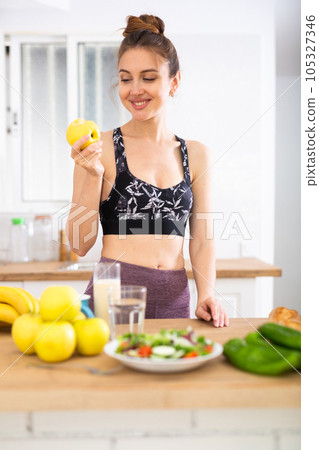 Slender sports girl eating apples in kitchen during breakfast Slender sports girl eating apples in kitchen during breakfast 105327346