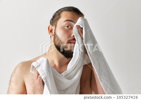 Photoshoot of man looking away and wiping towel after washing over light grey background. Photoshoot of man looking away and wiping towel after washing over light grey background. 105327419