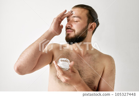 Handsome young man taking care of his skin over grey studio background. Bearded man. 105327448