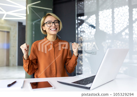 Young joyful business woman boss smiling and looking at camera, employee celebrating victory and successful achievement results looking at camera holding hands up triumph gesture. Young joyful business woman boss smiling and looking at camera, employee celebrating victory and successful achievement results looking at camera holding hands up triumph gesture. 105329294