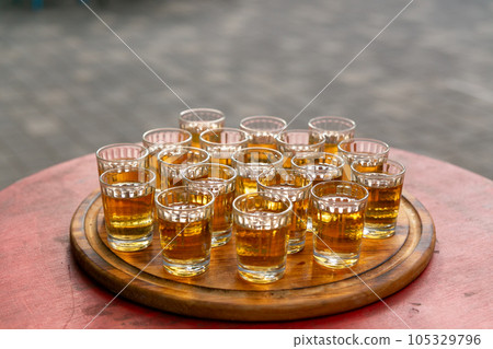 Small glasses filled with brandy on a wooden tray. 105329796