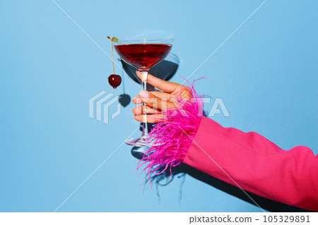 Women hand holding glass with drunk cherry cocktail over blue pop art background. Copy space for ad. Women hand holding glass with drunk cherry cocktail over blue pop art background. Copy space for ad. 105329891