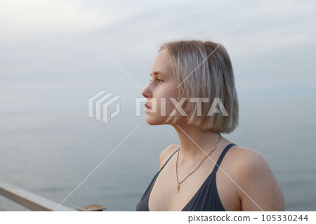 Portrait of woman in tank top standing on the background of sea and cloudy sky 105330244
