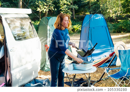 Middle age nomad woman washes dishes outside her camper van in forest camp during road trip. Enjoying free lifestyle, travel vacation. Weekend trip activity. Caravan car Vacation. Selective focus. Middle age nomad woman washes dishes outside her camper van in forest camp during road trip. Enjoying free lifestyle, travel vacation. Weekend trip activity. Caravan car Vacation. Selective focus. 105330280