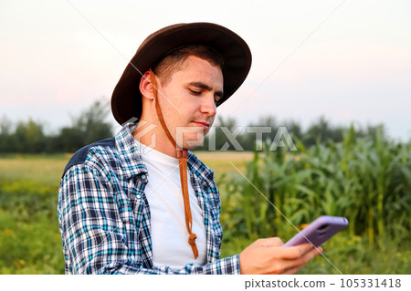 Farmer using phone. a dedicated farmer stands, attentively examining the crops that have emerged after sowing Farmer using phone. a dedicated farmer stands, attentively examining the crops that have emerged after sowing 105331418