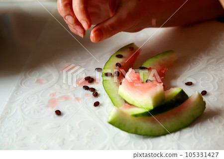 A woman enjoys a delicious watermelon, holding a slice in her hand at home. The close-up captures the vibrant colors and juicy texture of the fruit. After food. Out of focus 105331427