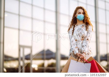 Woman in shopping. Young girl in protective sterile medical mask on her face with shopping bags. Woman in shopping. Young girl in protective sterile medical mask on her face with shopping bags. 105332097