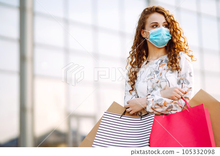 Woman in shopping. Young girl in protective sterile medical mask on her face with shopping bags. 105332098