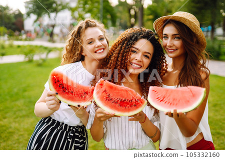 Three young woman have fun together and eating watermelon in hot summer day. 105332160