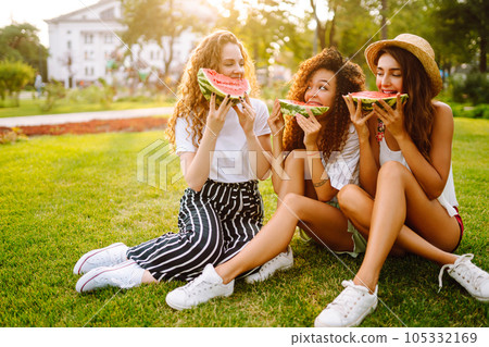 Cheerful happy friends camping on the grass, eating watermelon, laughing. 105332169