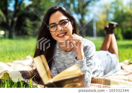 Beautiful relaxed woman readingbook at lawn with sun shining. Girl gets pleasure from reading book. Beautiful relaxed woman readingbook at lawn with sun shining. Girl gets pleasure from reading book. 105332344