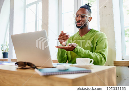 Young businessman, freelancer sitting at home and leading online video call via laptop with colleagues, discussion of projects 105333163