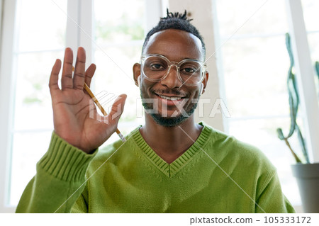 Young african man in glasses sitting at home, working studying. Online video call. Man waving at camera 105333172
