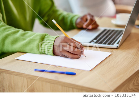 Close-up of male hands making notes with pencil on notebook,. working and studying online with laptop. Man sitting at table Close-up of male hands making notes with pencil on notebook,. working and studying online with laptop. Man sitting at table 105333174