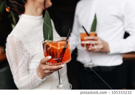 hands of woman and man are clinking, cheers with glasses of Spritz cocktail. Couple celebrating wedding, anniversary with Aperol spritz cocktails, with orange and greens Refreshing alcoholic drink hands of woman and man are clinking, cheers with glasses of Spritz cocktail. Couple celebrating wedding, anniversary with Aperol spritz cocktails, with orange and greens Refreshing alcoholic drink 105333232