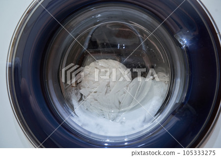 Wet white laundry in the drum of the washing machine. Close-up glass door from the washing machine with space for copying. High quality photo 105333275