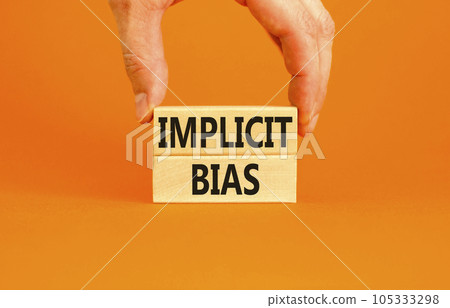 Implicit bias symbol. Concept words Implicit bias on wooden block. Beautiful orange table orange background. Businessman hand. Business psychology implicit bias concept. Copy space. 105333298