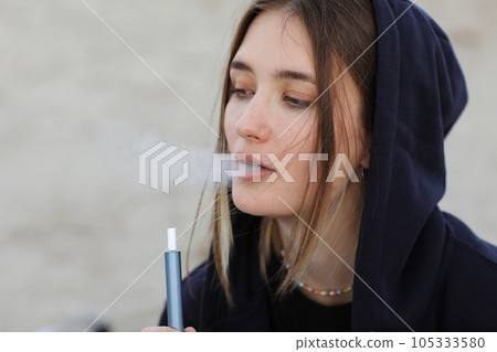 Electronic cigarette technology. Young woman smokes and releases steam from hybrid cigarette device that uses real tobacco refills with a heating pad, tobacco heating system. Bad unhealthy habit 105333580