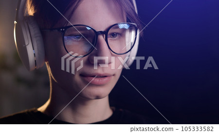 Young gamer man in glasses with screen reflection and headphones streaming live action game while explaining gameplay to subscribers. Gaming, esports, internet and virtual games at dark room 105333582