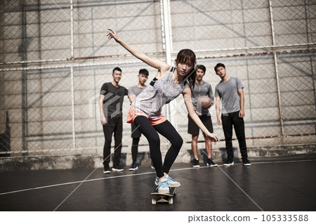 young asian woman skateboarder skateboarding outdoors with friends watching from behind young asian woman skateboarder skateboarding outdoors with friends watching from behind 105333588