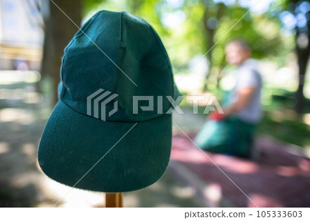A construction worker's green baseball cap hangs on a wooden peg. 105333603