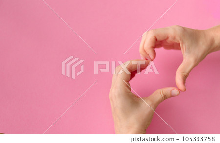 Women's hands in the shape of a heart on a pink background with space for text. High quality photo 105333758