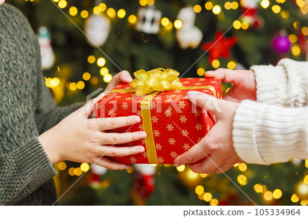 Hands of parent giving Christmas gift to child on Christmas tree background 105334964