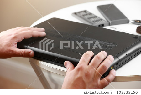 Repairman's hands removing the power battery from the laptop. Computer service and repair concept. Laptop disassembling in repair shop. Electronic development, electronic device fixing. 105335150