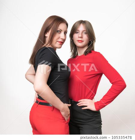 Adult mother in black t-shirt and red trousers, teenager daughter on contrary in red t-shirt and black trousers. Togetherness concept. Studio shot on white background. Part of photo series Adult mother in black t-shirt and red trousers, teenager daughter on contrary in red t-shirt and black trousers. Togetherness concept. Studio shot on white background. Part of photo series 105335478