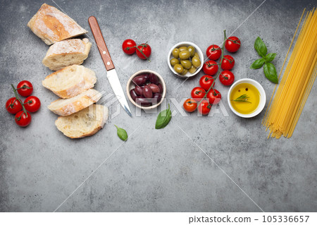 Food composition with sliced ciabatta, olives, olive oil, spaghetti, fresh basil, cherry tomatoes on gray concrete stone rustic background top view, space for text. Italian cuisine concept Food composition with sliced ciabatta, olives, olive oil, spaghetti, fresh basil, cherry tomatoes on gray concrete stone rustic background top view, space for text. Italian cuisine concept 105336657