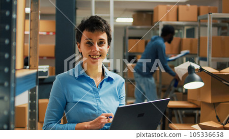 Female worker checking cardboard packages from storage room racks, using laptop to plan stock inventory and take notes. Entrepreneur working on business development and supply chain. Female worker checking cardboard packages from storage room racks, using laptop to plan stock inventory and take notes. Entrepreneur working on business development and supply chain. 105336658