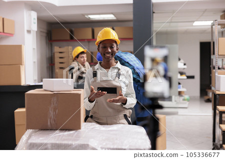 Woman taking smartphone video with customer order packing in retail storehouse. Smiling ecommerce shop warehouse worker looking at mobile phone camera and showing parcel preparation for dispatching 105336677
