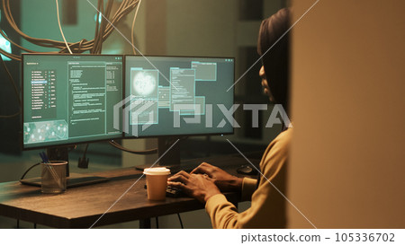 African american spy doing illegal security breach at night, working on cyberbullying to break computer firewall. Male thief hacking system with virus encryption, making threats. African american spy doing illegal security breach at night, working on cyberbullying to break computer firewall. Male thief hacking system with virus encryption, making threats. 105336702