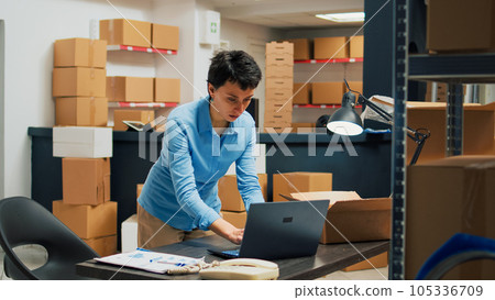 Caucasian woman putting merchandise in packages, working with laptop to do stock inventory before shipping products to customers. Female worker planning delivery management and logistics. Caucasian woman putting merchandise in packages, working with laptop to do stock inventory before shipping products to customers. Female worker planning delivery management and logistics. 105336709