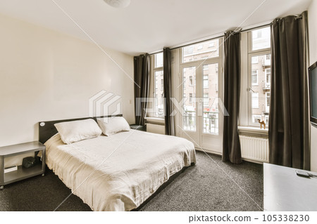 a bedroom with a bed, tv and large window overlooking the street in front of the apartment's windows 105338230